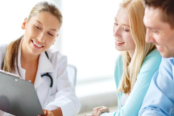 smiling female doctor with clipboard and patients in hospital