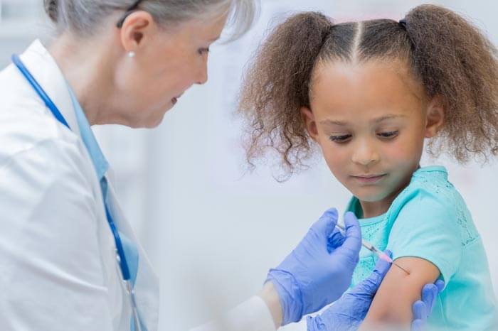 Senior pediatrician gives a young female patient a shot in the arm.