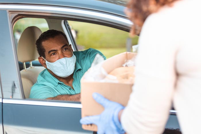 During the coronavirus epidemic a mature adult man wears a mask while receiving a box of food.