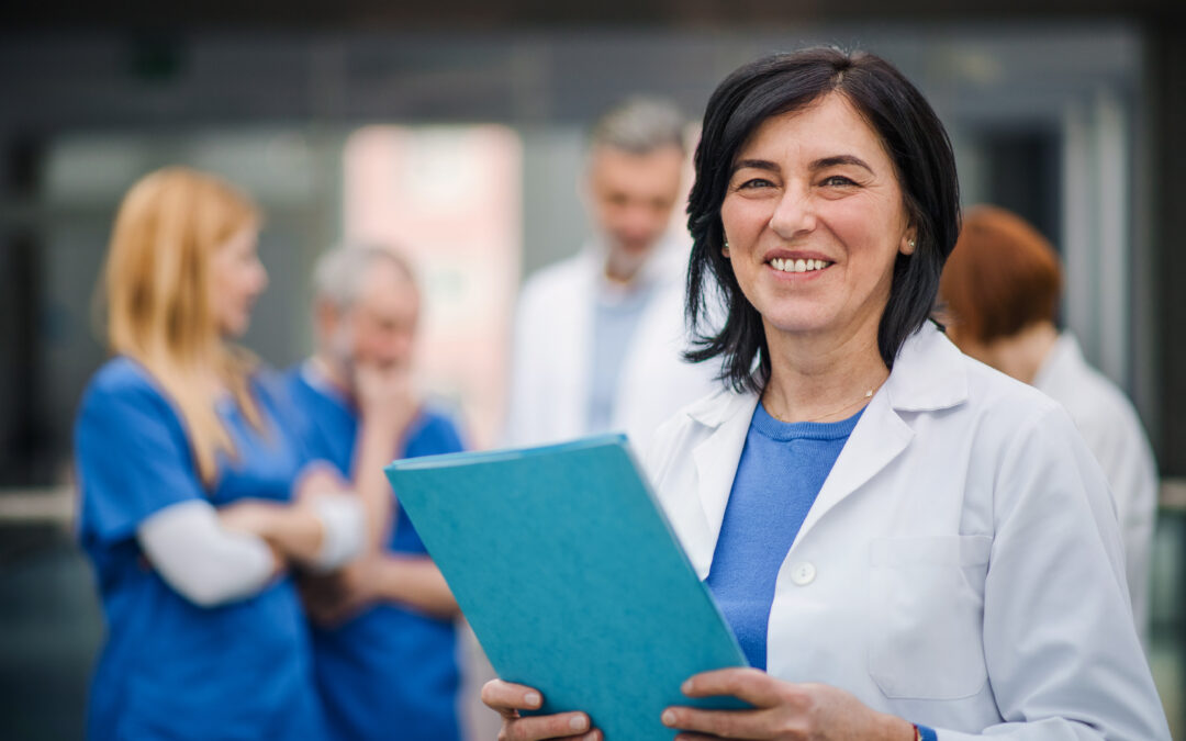 An image of a smiling doctor with a clipboard who is about to start TrueCare's performance review process with an employee.