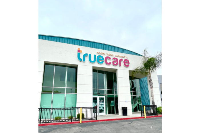 A picture of the outside of a beautiful Community Health Center, a white building with colored lettering and giant pane windows, which is just one reason to work at TrueCare San Marcos